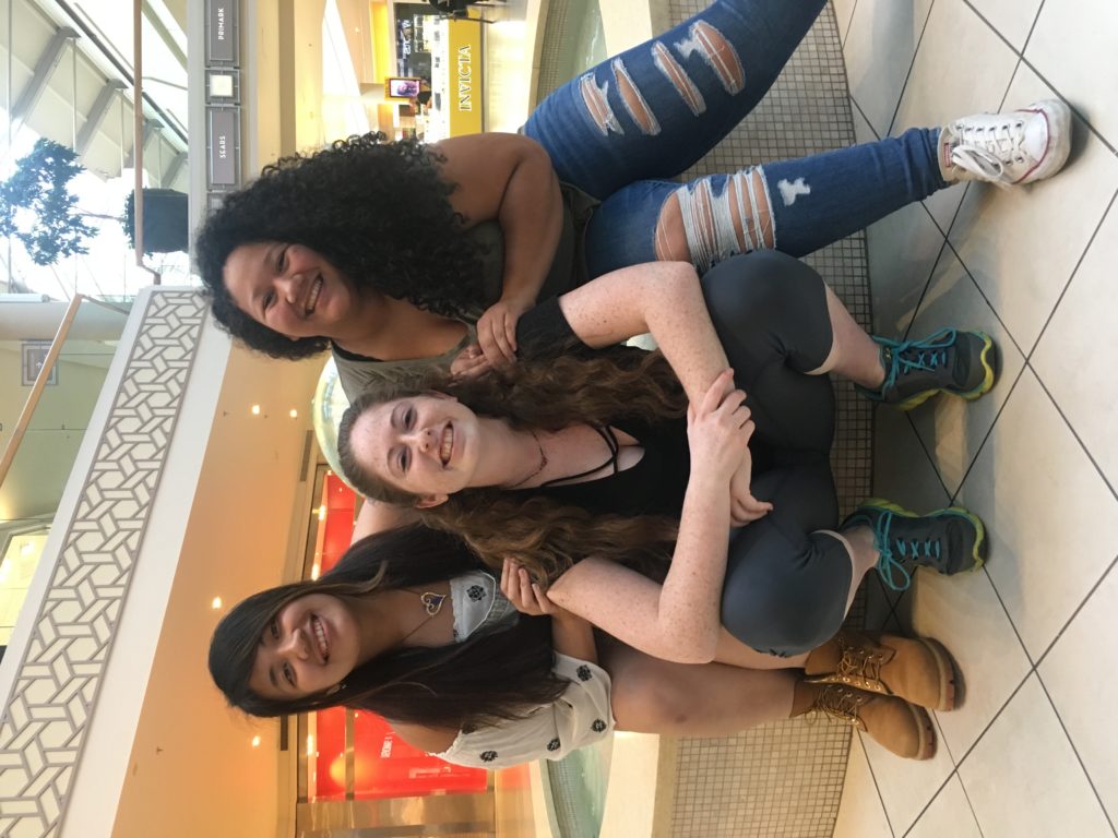 Three women sitting on a fountain in a mall