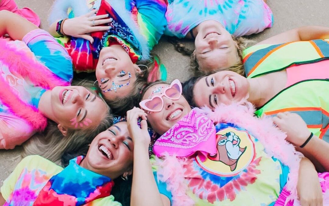 Sorority women on bid day laying down with their sisters and dressed in tie dye shirts and colorful accessories.